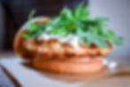 Close-up of a crispy chicken sandwich with arugula and white sauce on a bun. Brown and green tones dominate the appetizing scene.