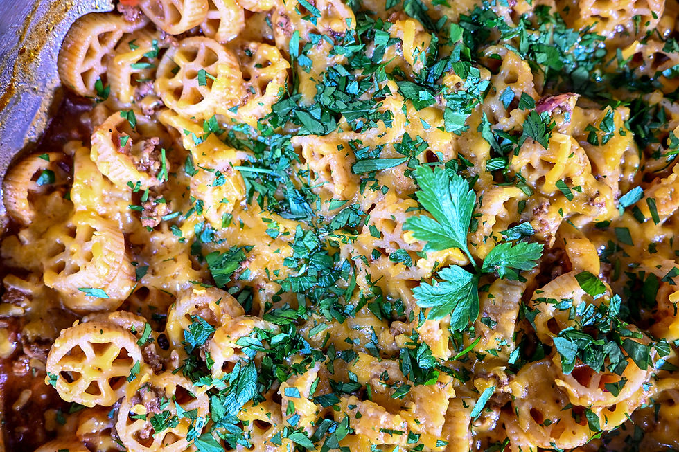 Close-up of cheesy wheel pasta topped with chopped herbs in a pan, warm golden-brown comfort food.