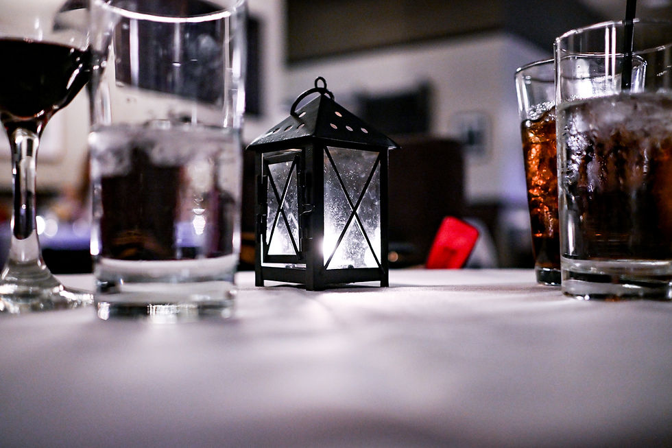 Tabletop with glasses of drinks and a small black lantern glowing softly. Blurred background suggests a cozy indoor setting.