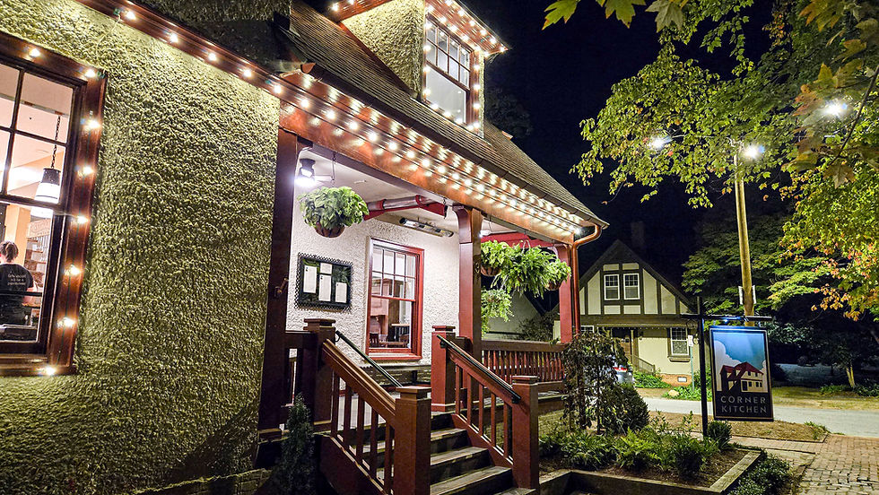 Cozy restaurant exterior at night, warm string lights, greenery hanging, visible "Corner Kitchen" sign. Inviting atmosphere.