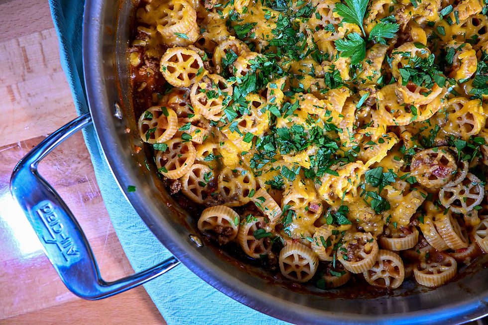 Overhead view of a skillet of cheesy baked pasta with parsley on a wooden table, warm and hearty with a blue cloth nearby