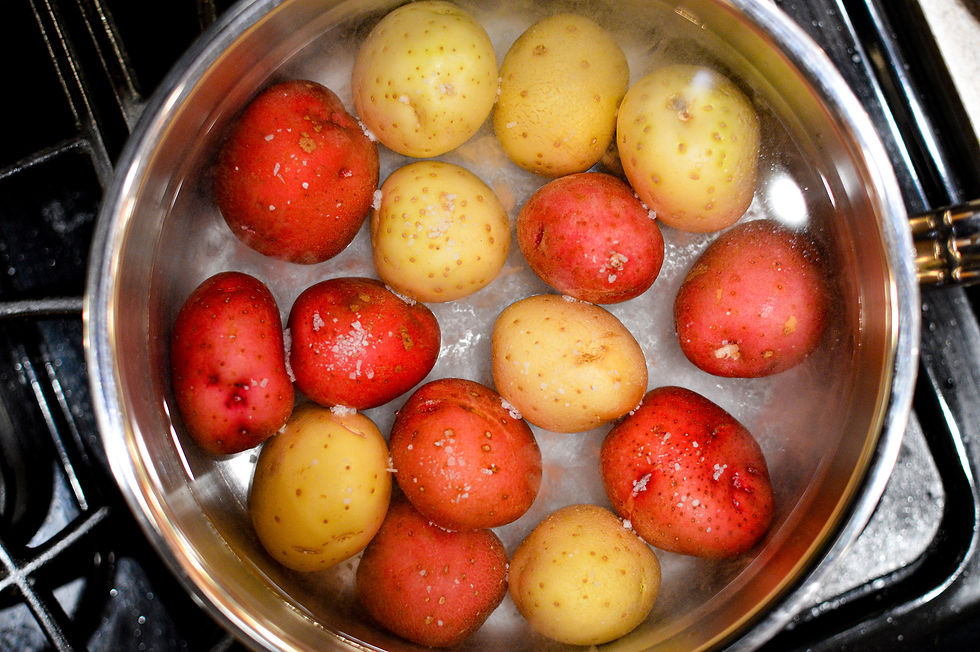Boiling red and yellow potatoes in a silver pot, with steam rising. Set on a stove, the scene captures a vibrant, home-cooking moment.