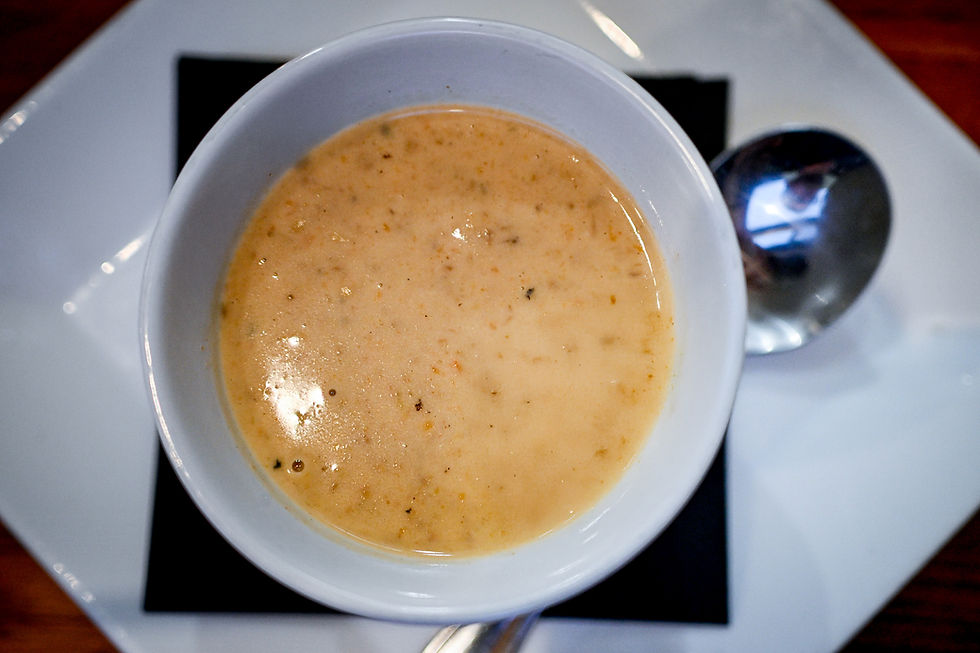 Creamy soup in a white bowl on a black napkin, placed on a white plate. A shiny spoon is nearby, creating a simple, cozy mood.