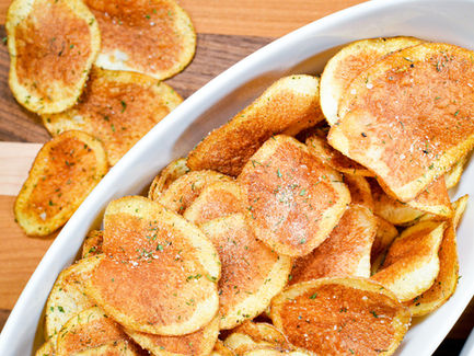 Crispy, seasoned chips are arranged in two white oval bowls on a wooden surface. The golden-brown chips have a sprinkle of herbs.