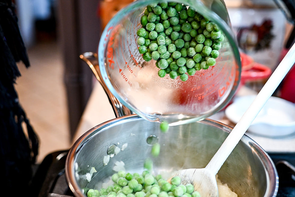 Green peas being poured from a glass measuring cup into a pot with a wooden spoon on a stove. Cooking setting, vibrant green color.
