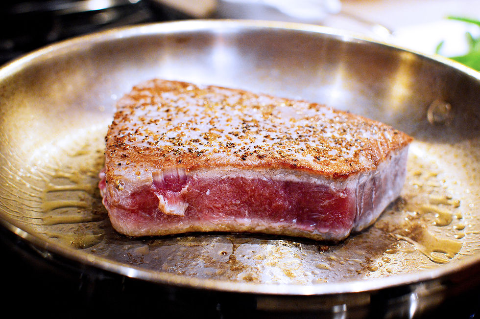 Seared tuna steak cooking in a hot skillet, with a seasoned crust. Golden brown edges and a shiny surface with oil droplets.