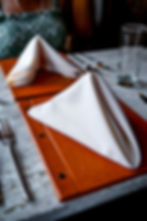 White napkins folded elegantly on brown menus with a fork and glass on a marble table. A person in a green patterned top is seated.