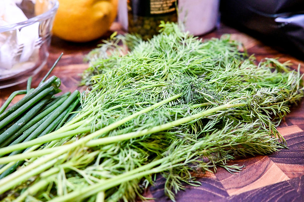 Fresh dill and chives on a kitchen counter, with a lemon and jar blurred in the background.