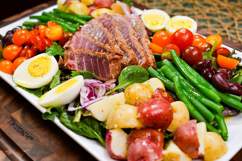 A colorful salad on a platter with seared tuna slices, boiled eggs, cherry tomatoes, green beans, potatoes, and greens. Text reads "TAMODACHI".