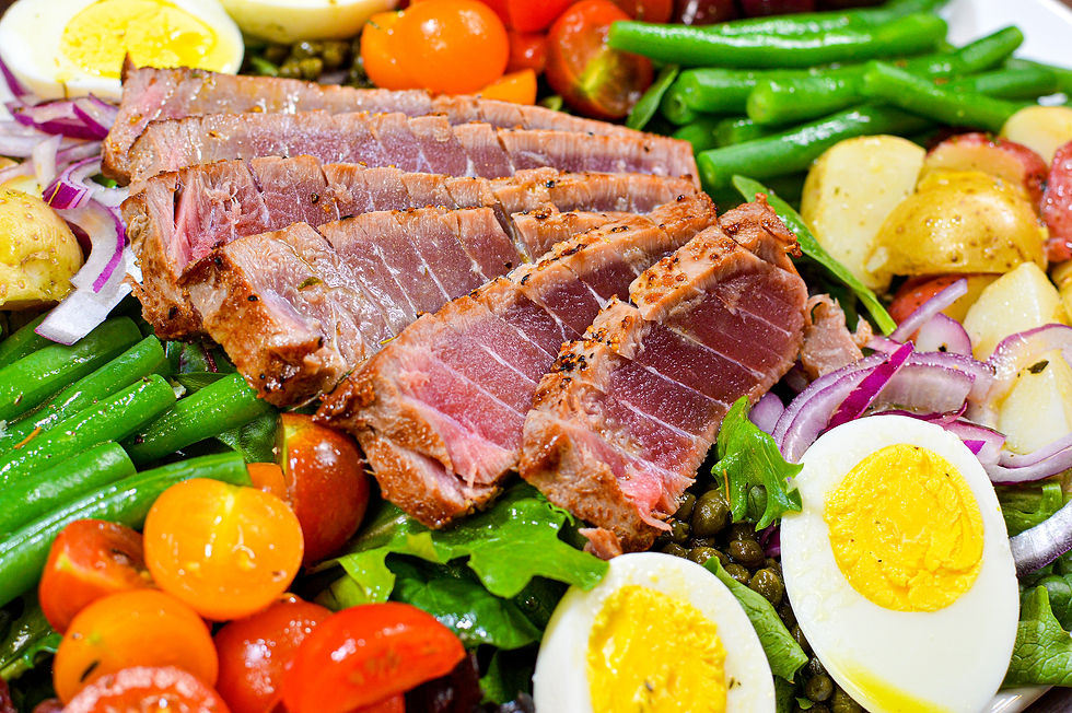 Slices of seared tuna on a colorful salad with cherry tomatoes, green beans, boiled eggs, and potatoes. Vibrant and fresh setting.