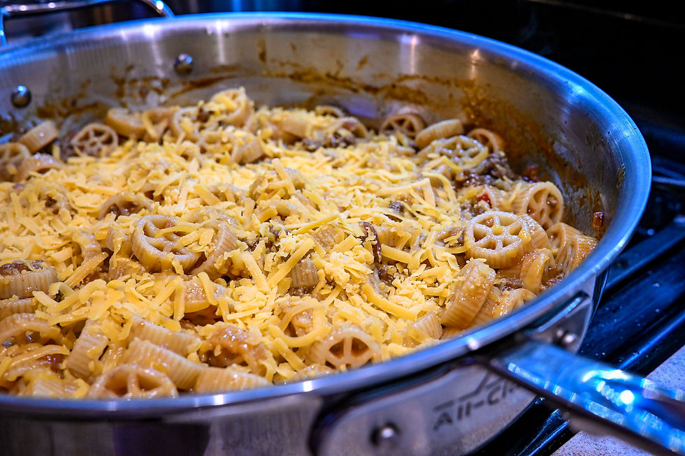 Pasta shells in a stainless steel skillet, topped with shredded cheese on a stovetop, with a warm, hearty feel.