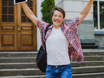Excited student with backpack cheering outside school