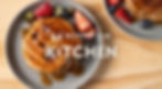 Pancakes drizzled with syrup on a gray plate, topped with strawberries and blueberries. Text reads "MYPROTEIN KITCHEN" on a wooden table.