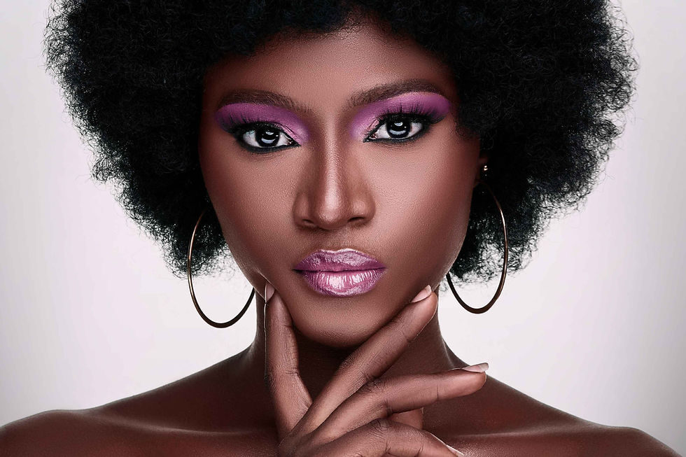 Close-up of a woman with afro hair, wearing purple makeup and hoop earrings. Her expression is confident, with a hand touching her chin. 2025 GLOBAL TRENDS: Beauty and Personal Care DiMotta Strategic Adriana Motta