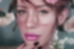 2025 GLOBAL TRENDS: Beauty and Personal Care DiMotta Strategic Adriana Motta. Close-up of a person with freckles and pink lips, touching their chin. Soft focus on flowers and teal background. Calm expression.