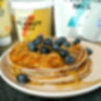 Pancakes topped with blueberries and syrup on a plate. Peanut butter and pancake mix containers in the background. Warm and inviting mood.