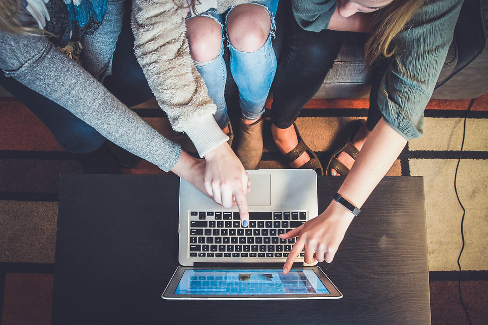 A group of three girls pointing to a laptop screen, measuring results of a marketing campaign.