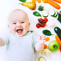 Mosolygó kisbaba bio zöldségek és gyümölcsök között, hozzátáplálásra készülve.