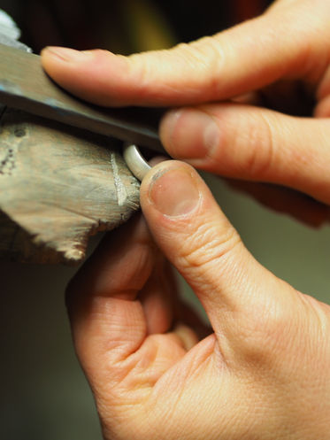 zwei Hände, die mit einer Feile einen Silberring bearbeiten