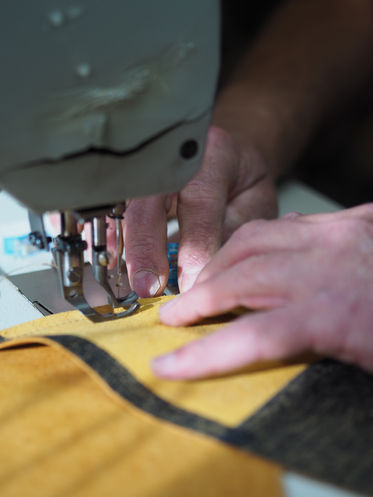 zwei Hände, die an der Nähmaschine Leder vernähen