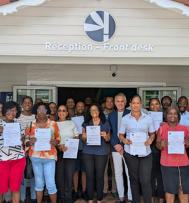 Eric Alauzen entouré des participants à une formation hôtelière au Bambou Resort, en Martinique, devant la réception de l’établissement, avec leurs attestations de formation.