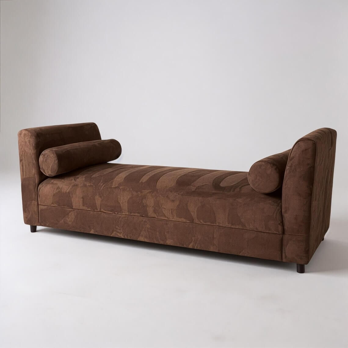 Brown velvet backless lounge with a subtle striped texture, curved end arms, and two bolster pillows.