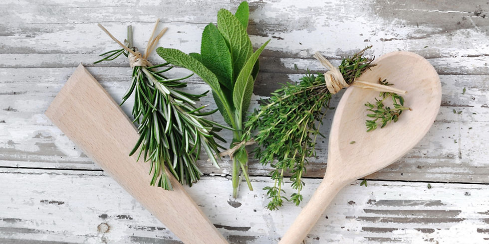 Frische Kräuterbündel aus Rosmarin, Salbei und Thymian neben einem Holzlöffel auf einer hellen rustikalen Oberfläche.