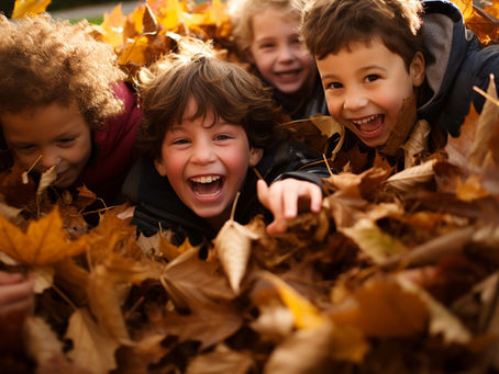 Vier lachende Kinder spielen ausgelassen in einem großen Haufen bunter Herbstblätter – ein fröhlicher Moment beim Naturerlebnis im Herbst.
