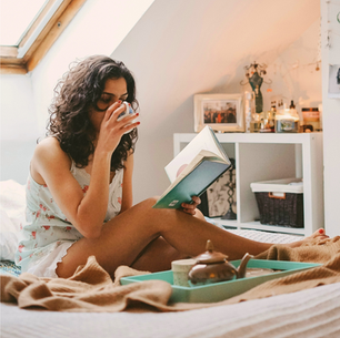 woman drinking tea while reading a book in bed