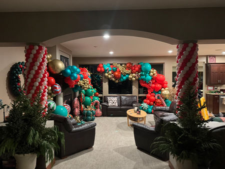 Side view of Christmas balloon décor with red, green, gold, and teal balloon garlands, candy cane spirals, and holiday accents decorating the event room