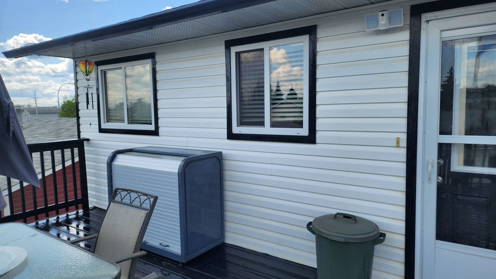 a green trash can sits next to a window on the side of a house