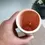 Thumbnail: Angled top view of one of the Shrimp Pink and white Ceramic Small Vases held in a hand