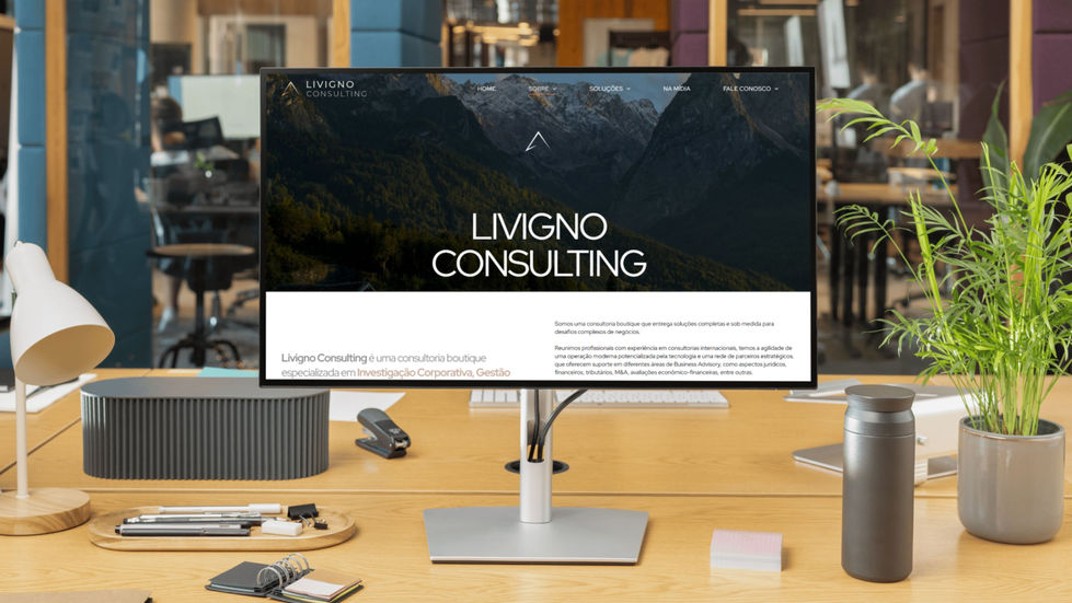 Monitor widescreen em uma mesa de escritório mostrando o site da Livigno com fotos de montanhas e tipografia branca.