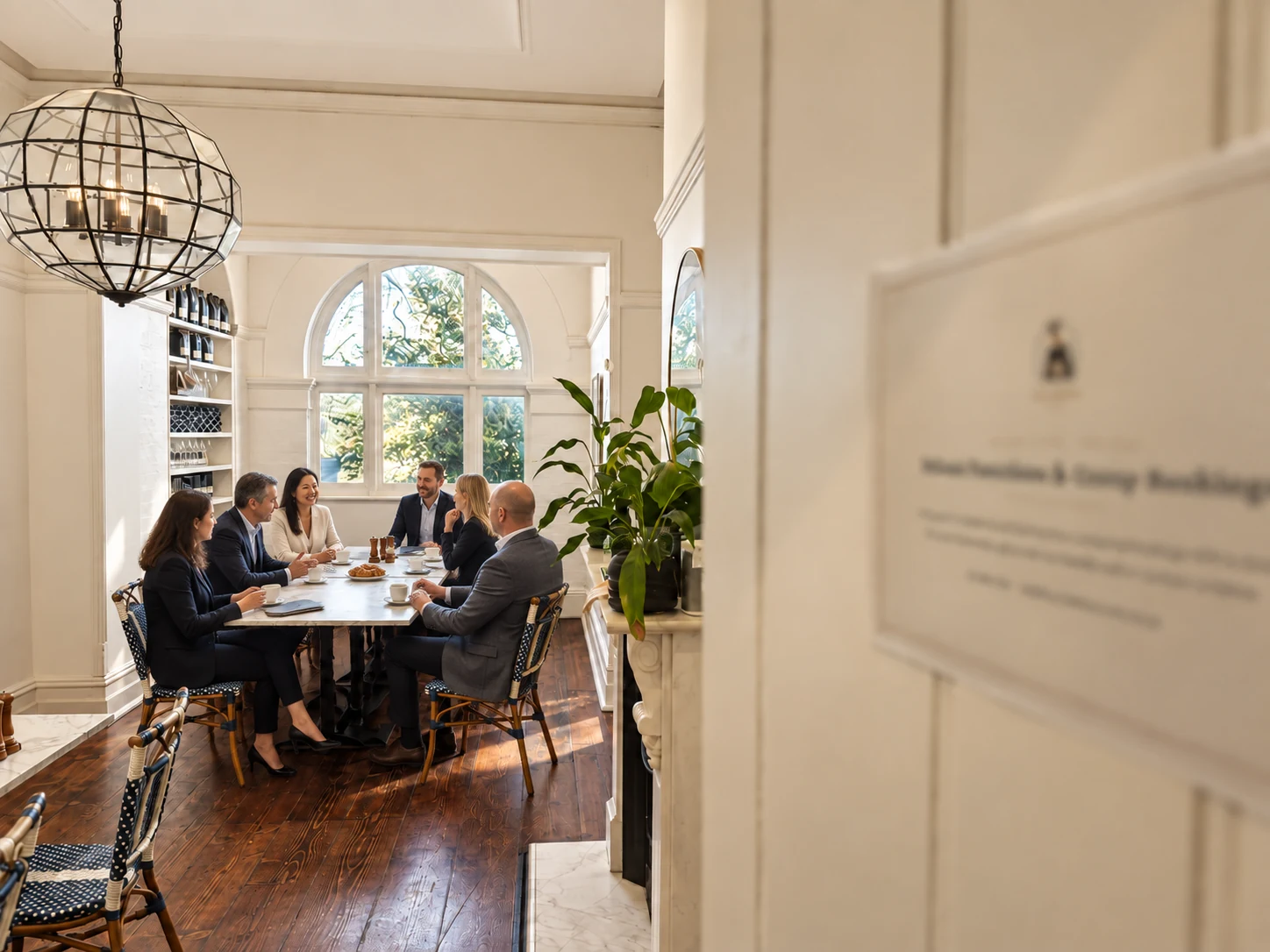 Corporate colleagues seated around the long table in the back room, viewed through the doorway