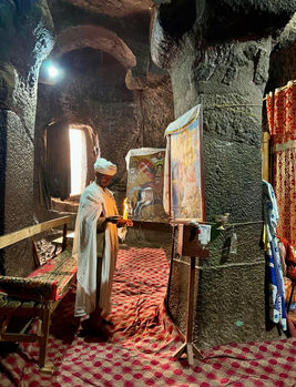 Priester hält Kerze, vor religiöser Kunst in einer Höhle. Innenraum mit Text.