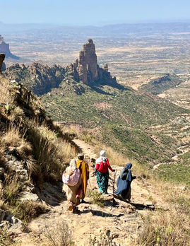 Drei Frauen wandern einen Pfad entlang; im Hintergrund Berg und Tal. Landschaft.