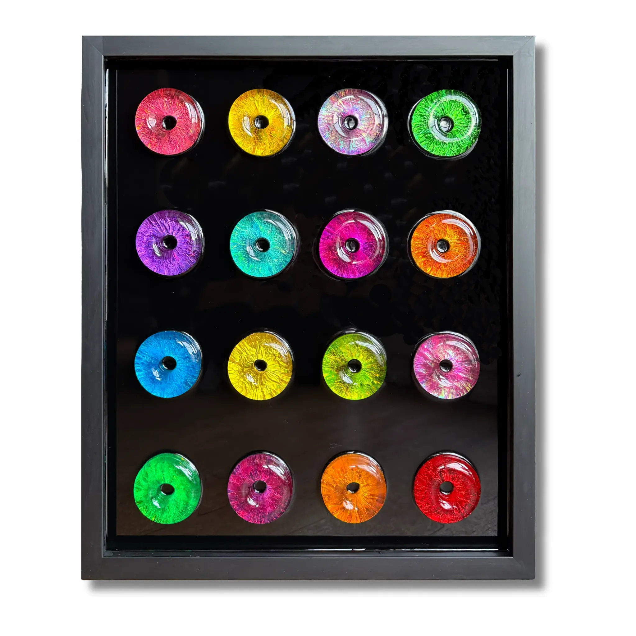 Colorful resin donut wall art arranged in a 4x4 grid on a glossy black background.
