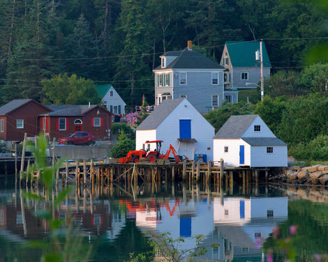 Bright white lobster sheds with deep blue doors reflect in the harbor water