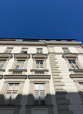Eine verzierte Fassade in weiß und grau in Wien, darüber blauer Himmel
