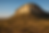 Rocky hill bathed in golden light rises from a savanna with scattered acacia trees under a clear blue sky, evoking a serene, timeless mood.