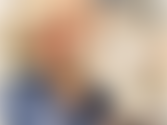 Woman smiling with short blonde hair, wearing a blue shirt. A small white dog with a red collar nuzzles her cheek. Outdoor, sunny day.