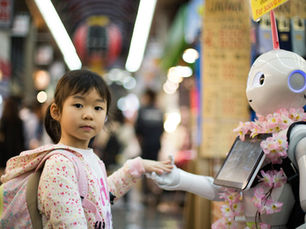 A child holds a robot's hand in a busy market. The robot wears a pink flower garland. Bright lights and colorful signs fill the background.