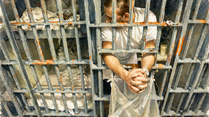 Man in white shirt leans outside prison cell bars, hands clasped. Worn bed and cup visible inside. Grungy, tense atmosphere.