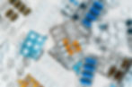 Various tablets and capsules in colorful blister packs scattered on a white surface, featuring blue, orange, and white pills.