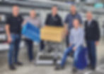 Stefan Maßmann, Jürgen Bolte, and Dimitri Kool (all Beckhoff systems engineering team), Maximilian Budde (seated) and Tristan Rodewald (both Budde Systems), and Markus Wolharn (Arvato SE) – from left to right – in front of the ring conveyor mounted under the ceiling with one of the 27 control cabinets for supplying the EP7402 MDR controllers. © Beckhoff