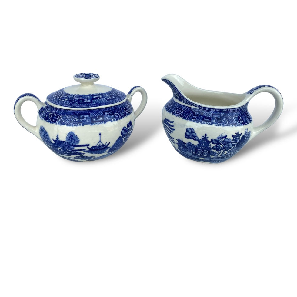 A set of vintage blue willow chinaware featuring a lidded sugar bowl and a creamer pitcher. Both pieces are adorned with intr
