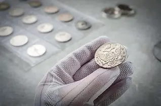 Gloved hand holding an old coin