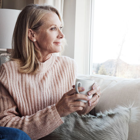 A peaceful moment of a woman sitting by a window with a cup of coffee, representing caregiver self-care.