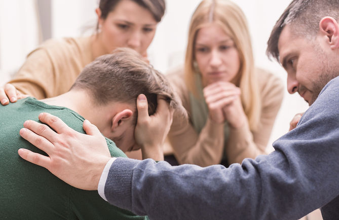 Close-up of a devastated young man holding his head in his hands and friends supporting hi
