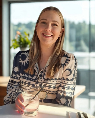 Lisa seated at a cafe table, wearing a patterned dress, with a blurred background view.